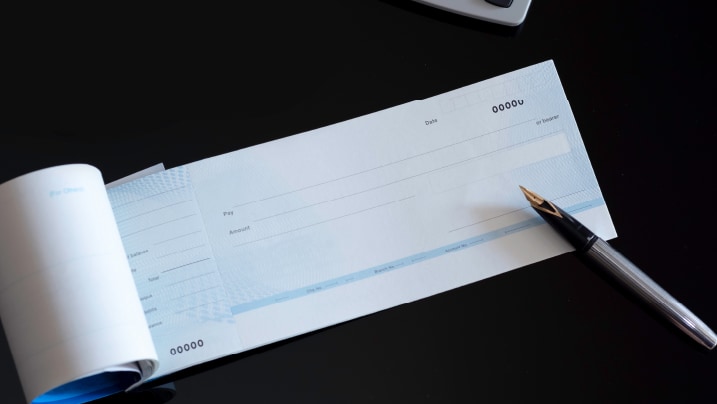 A cheque book placed on a desk alongside a pen and financial documents.